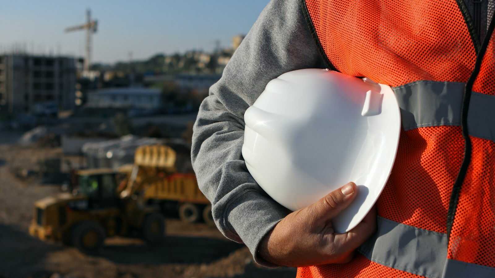 Aannemer en architect bekijken bouwplannen op werf met dakconstructie in aanbouw